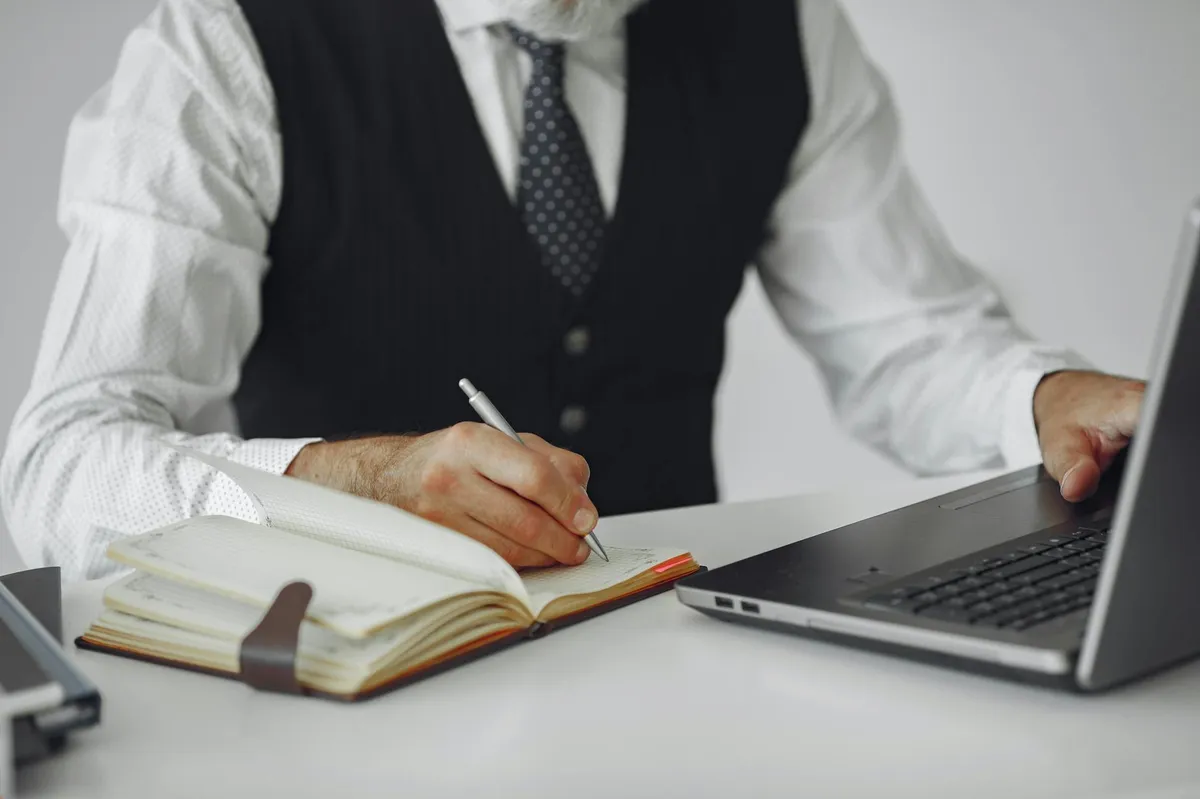 Pessoa com caderno aberto anotando informações sobre o negócio antes de usar o computador