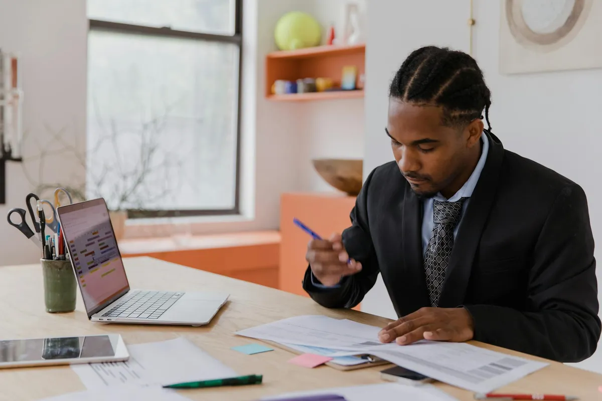 Empresário em escritório olhando para laptop com documentos e relatórios de negócio na mesa